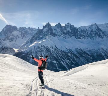 Personne de dos descendant une piste en snowboard les bras en l'air