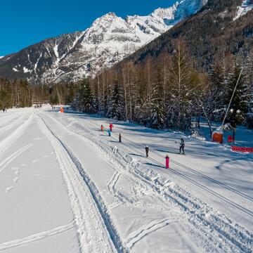 Large piste de ski nordique où des élèves apprennent à skier auprès d'un professeur